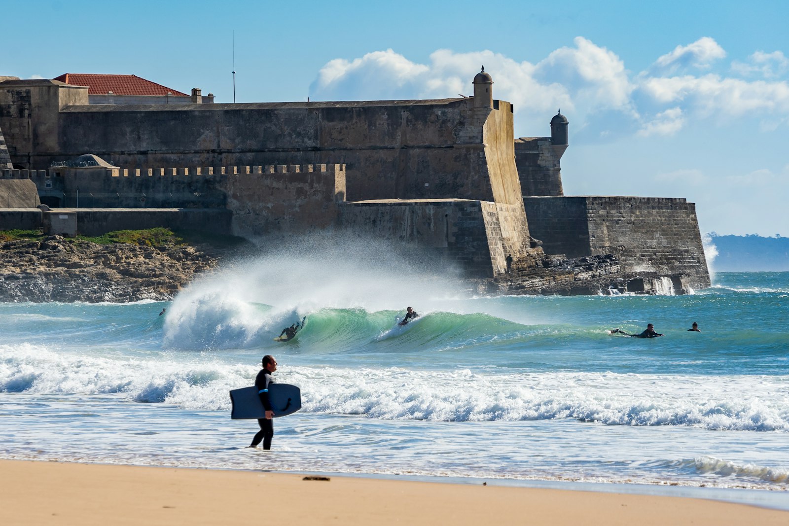 A surfer on the beach near the fort in Nazaré, Portugal